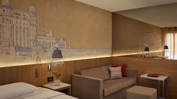 Quarto de hotel com um grande mural de um edifício histórico, um sofá, uma mesa pequena e uma mesa de cabeceira com uma luminária.