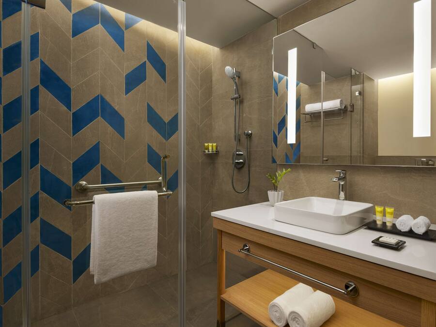 Un baño moderno con cabina de ducha de vidrio, un lavabo blanco y un mueble de tocador de madera.
