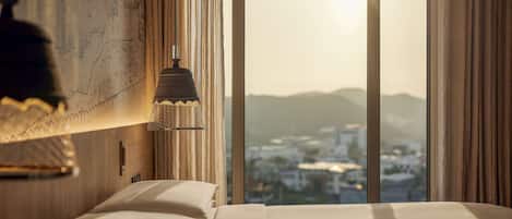 A hotel room with a large bed, a map on the wall, and a view of a cityscape through the window.