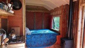 A rustic cabin interior with a bed, a stove, and a window. - Totnes - Cabin - Sleeps 4 - Garden - Parking (Totnes)