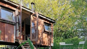 A rustic cabin with a wooden exterior, a chimney, and a set of outdoor chairs. - Totnes - Cabin - Sleeps 4 - Garden - Parking (Totnes)