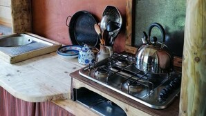 A rustic kitchen with a gas stove, a kettle, and various kitchen utensils. - Totnes - Cabin - Sleeps 4 - Garden - Parking (Totnes)