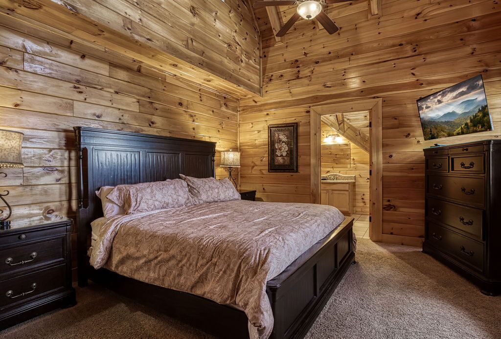 A wooden-paneled bedroom with a bed, nightstands, a dresser, and a ceiling fan.