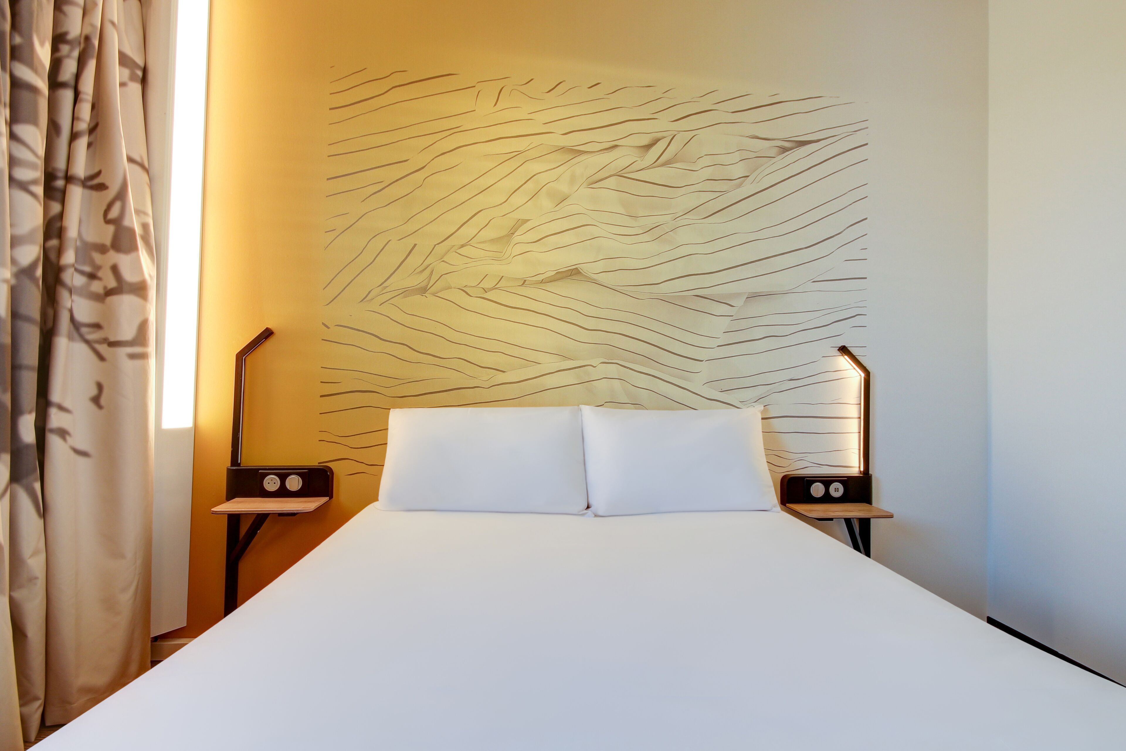 A hotel room with a bed, two bedside tables, and a wall with a wavy pattern.