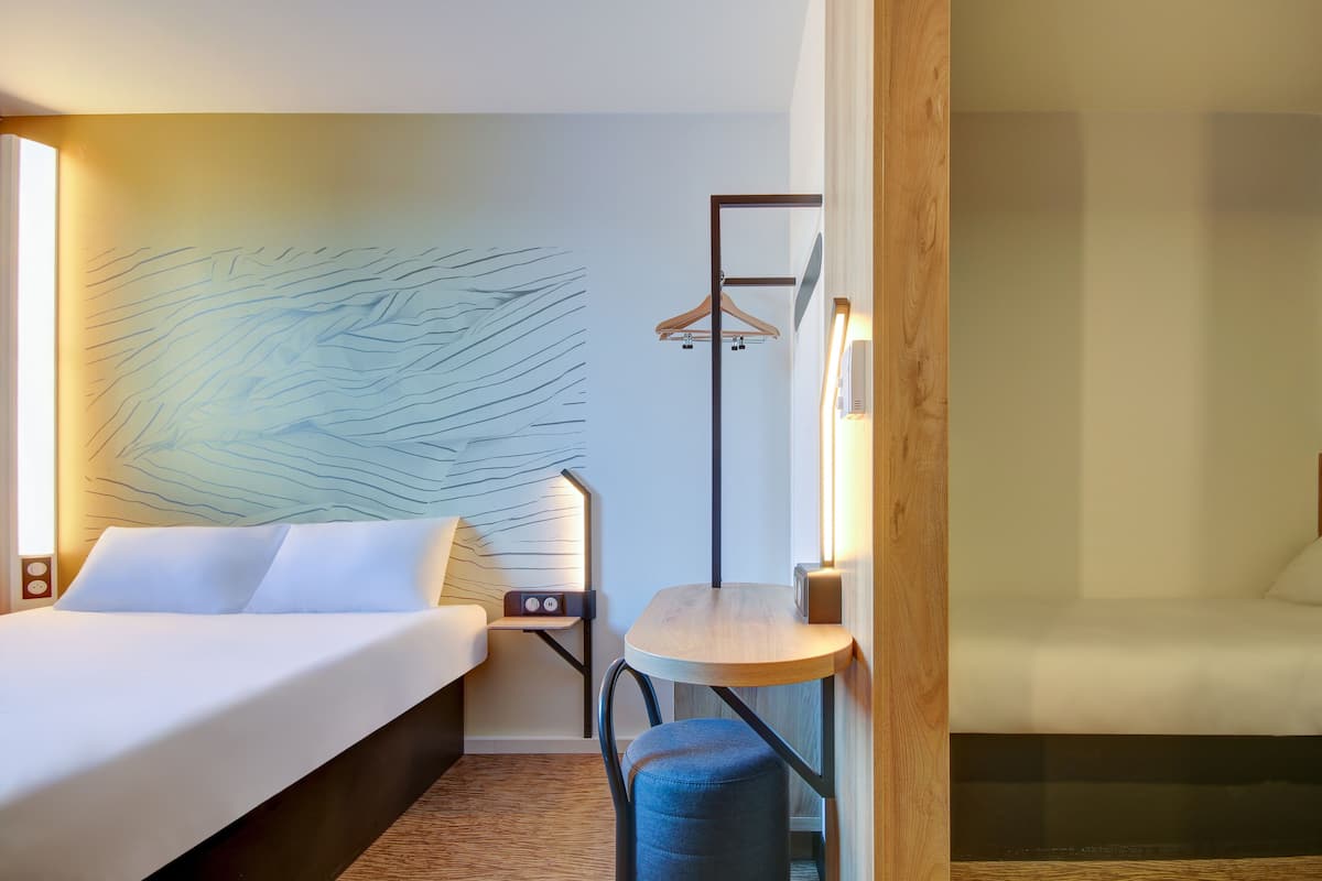 A hotel room with a bed, a small table, a chair, a wall-mounted coat rack, and a wall with a textured design.