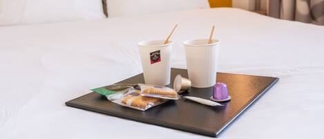 Una bandeja con dos tazas, un cepillo de dientes, una pastilla de jabón y un paquete de snacks sobre una cama.