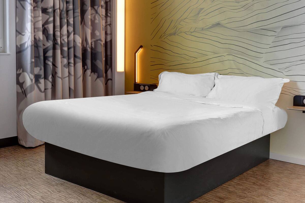 A modern hotel room with a large bed, a nightstand with a lamp, and a wall with a unique textured design.