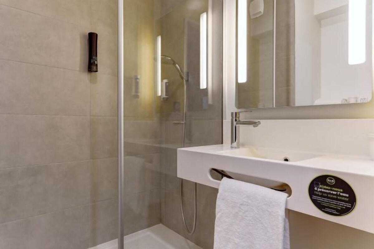 A modern bathroom with a glass shower enclosure, a white sink, and a towel rack.
