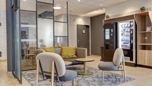 A modern lounge area with a sofa, two armchairs, a small coffee table, and a vending machine. - B&B HOTEL Epernay (Epernay)