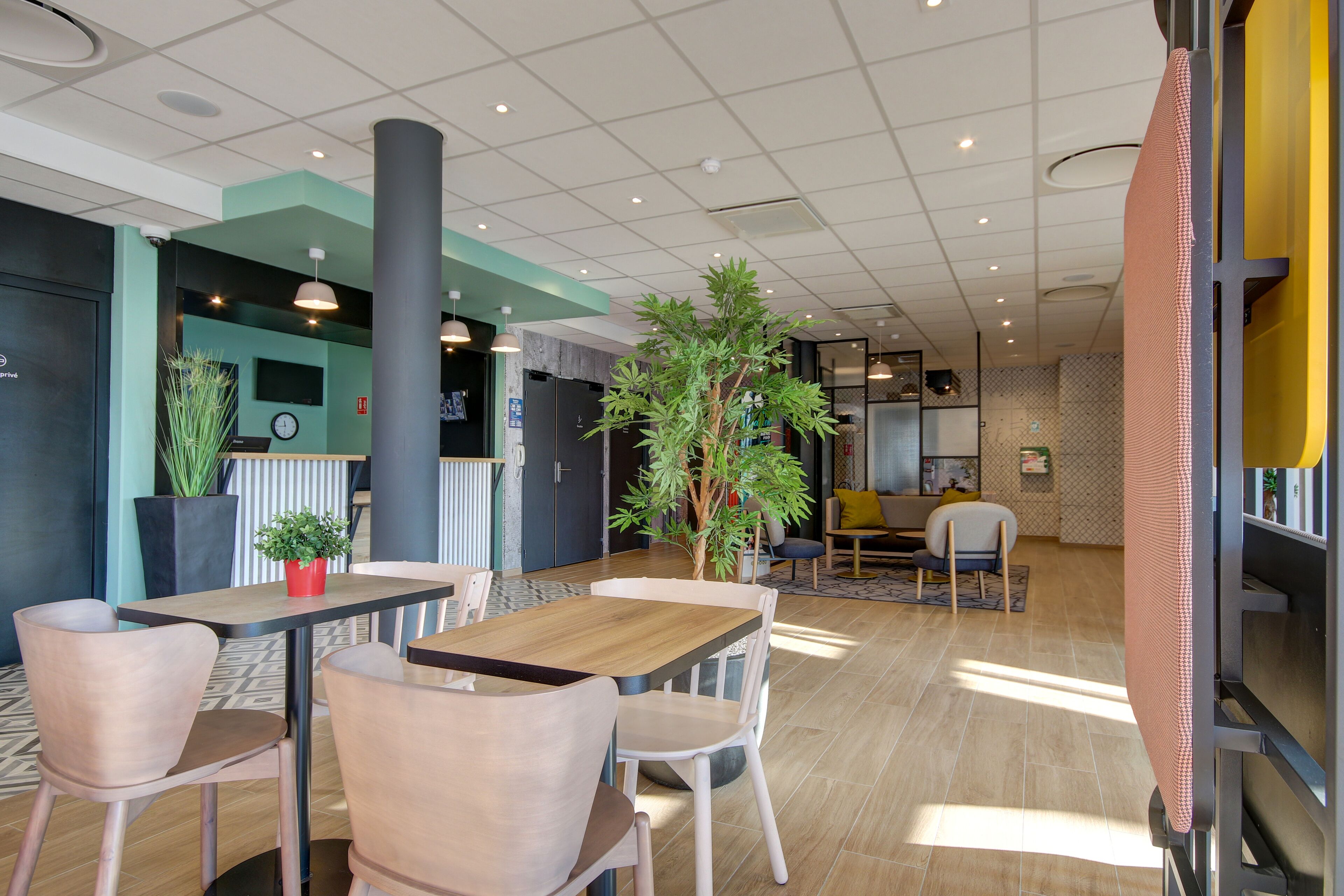 A modern indoor space with tables and chairs, a large pillar, and potted plants.