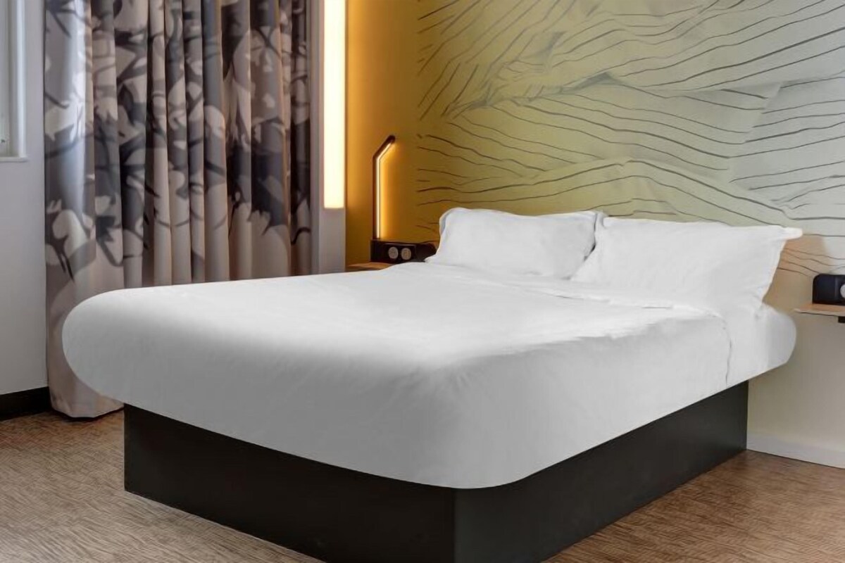 A modern bed with a white mattress and dark base, a wall with a leaf pattern, and a lamp on the nightstand.