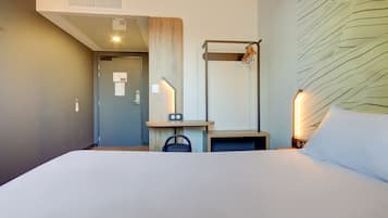 A hotel room with a bed, a desk, a chair, a mirror, and a wall with a textured design.