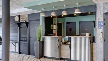 Un espace d’accueil au design moderne, comprenant un comptoir de réception, une grande plante en pot et un téléphone fixé au mur.