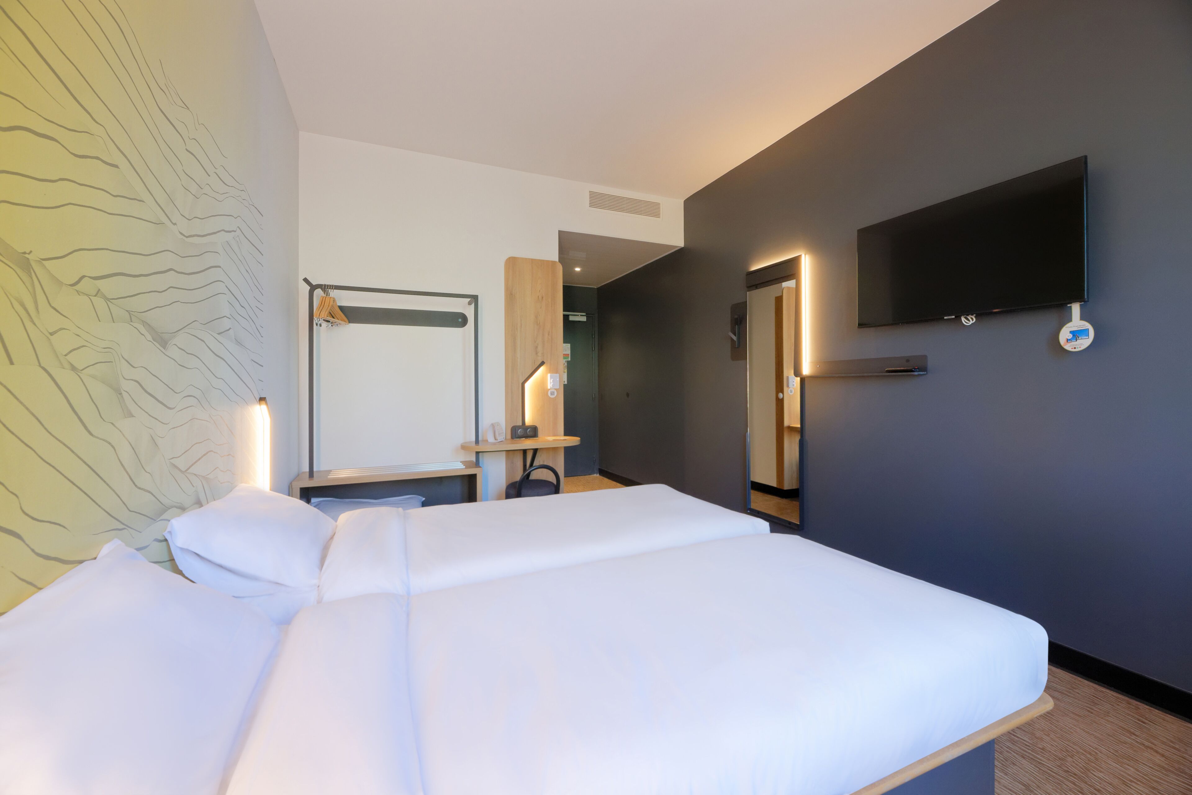 A hotel room with a bed, a desk, a flat-screen TV mounted on the wall, and a mirror.