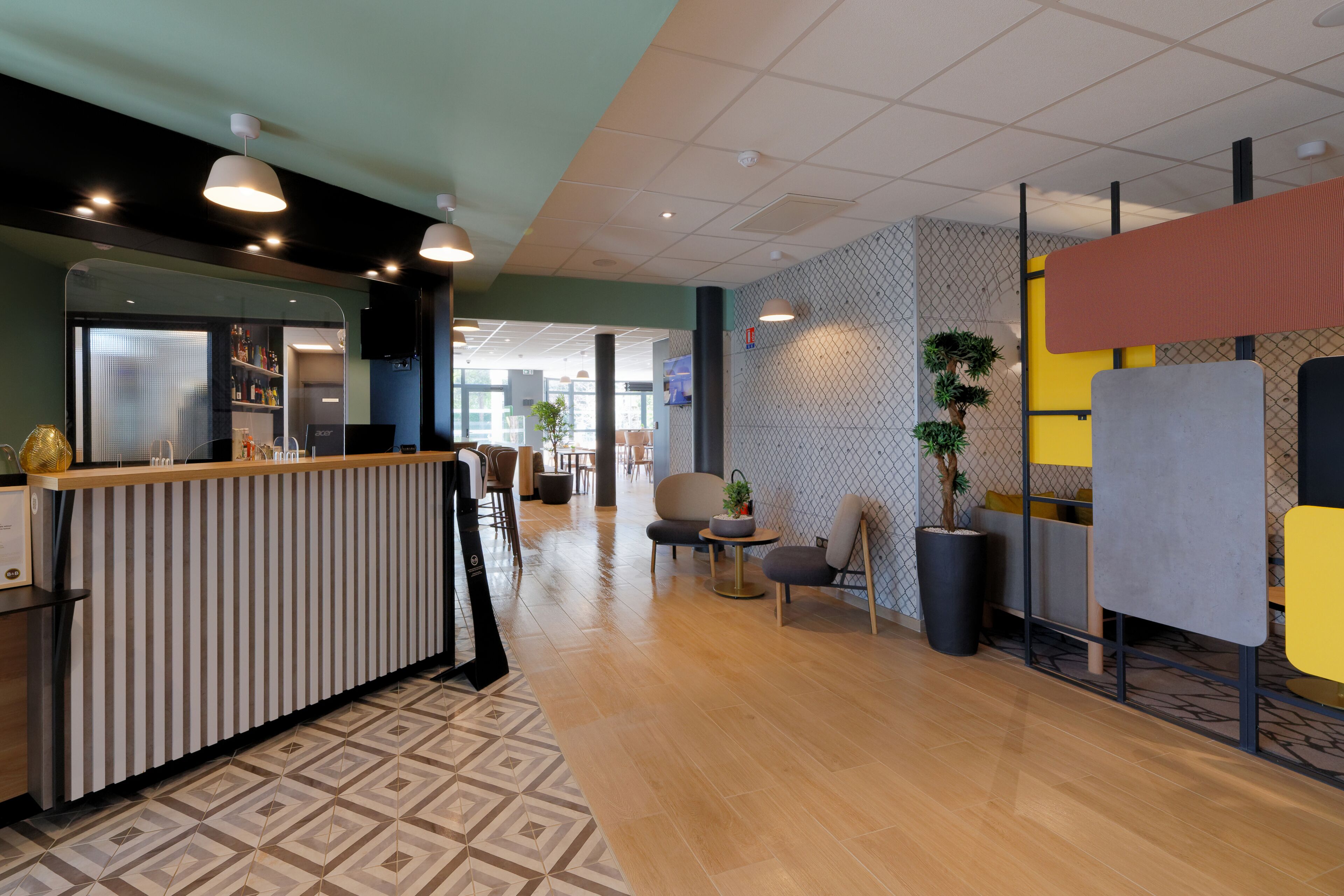 A modern hotel lobby with a reception desk, seating area, and a large potted plant.