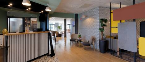 A modern hotel lobby with a reception desk, seating area, and a large potted plant.