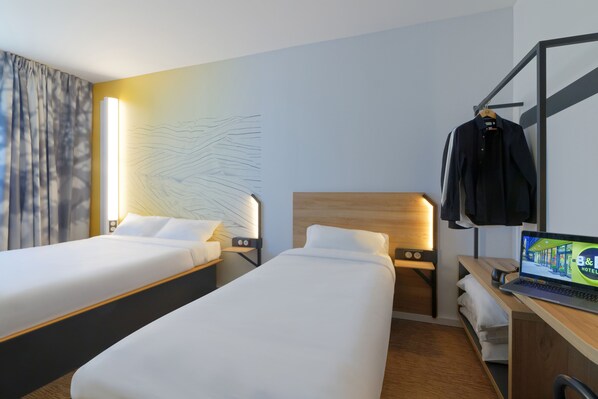 A hotel room with two beds, a desk with a laptop, and a coat rack. - B&B HOTEL Le Touquet (Cucq)