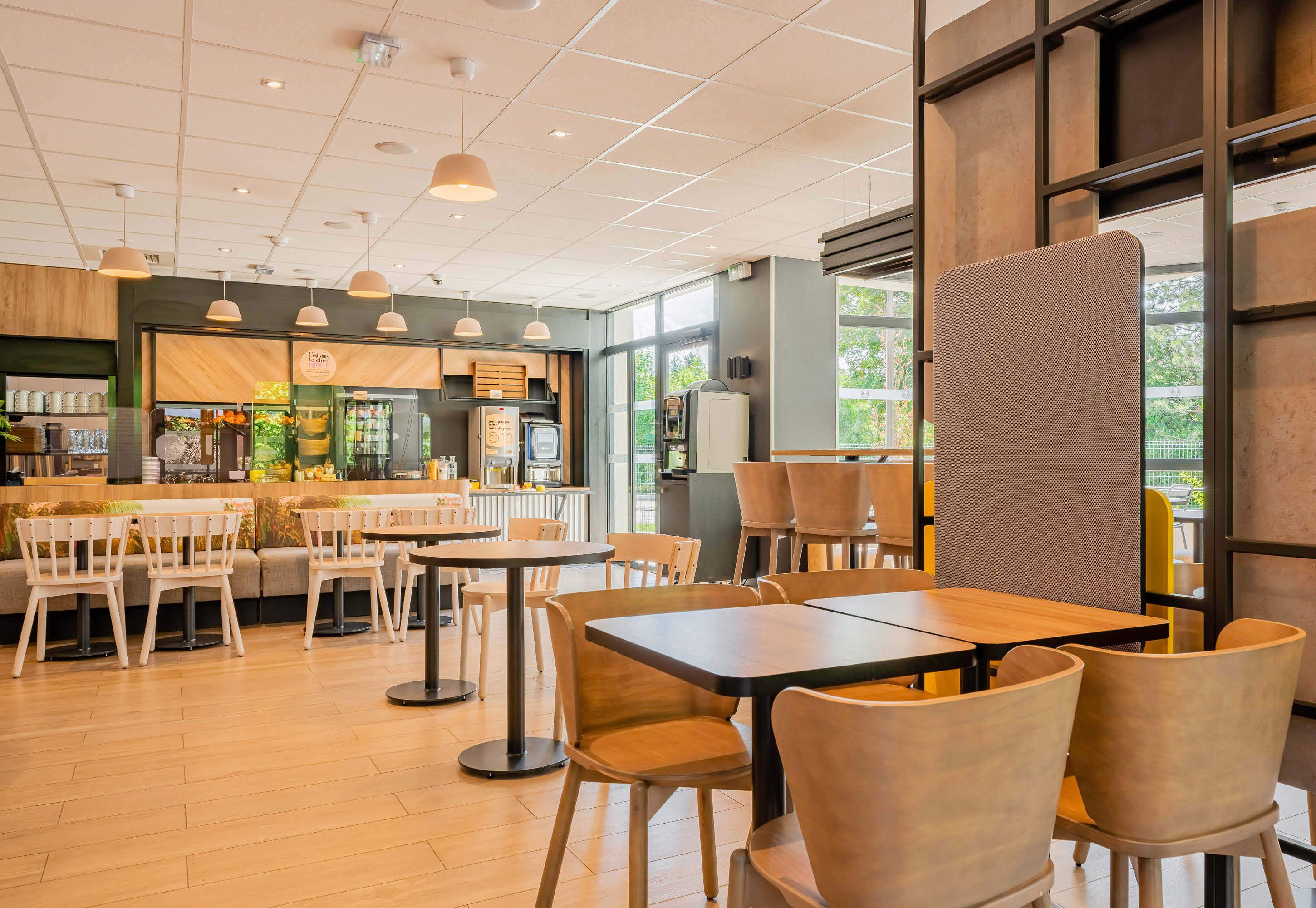 Un café moderno con suelo de madera, mesas redondas y sillas con cojines.