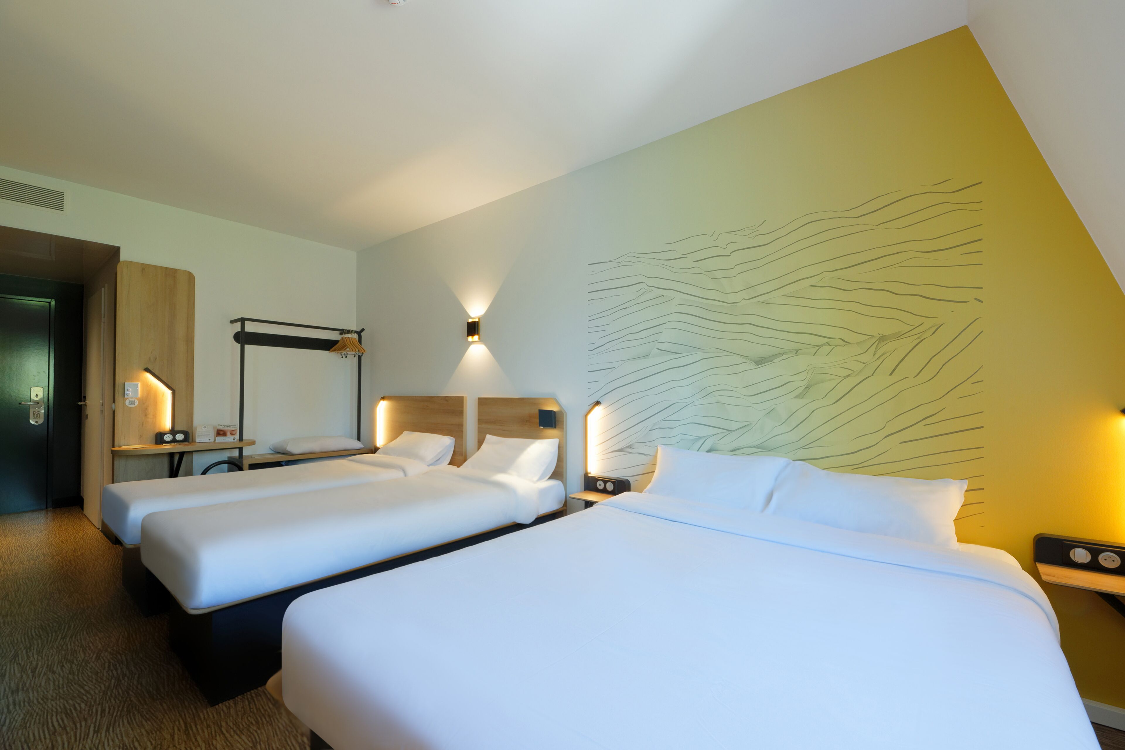A hotel room with two beds, a wooden headboard, bedside tables with lamps, and a wall with a leaf-like design.