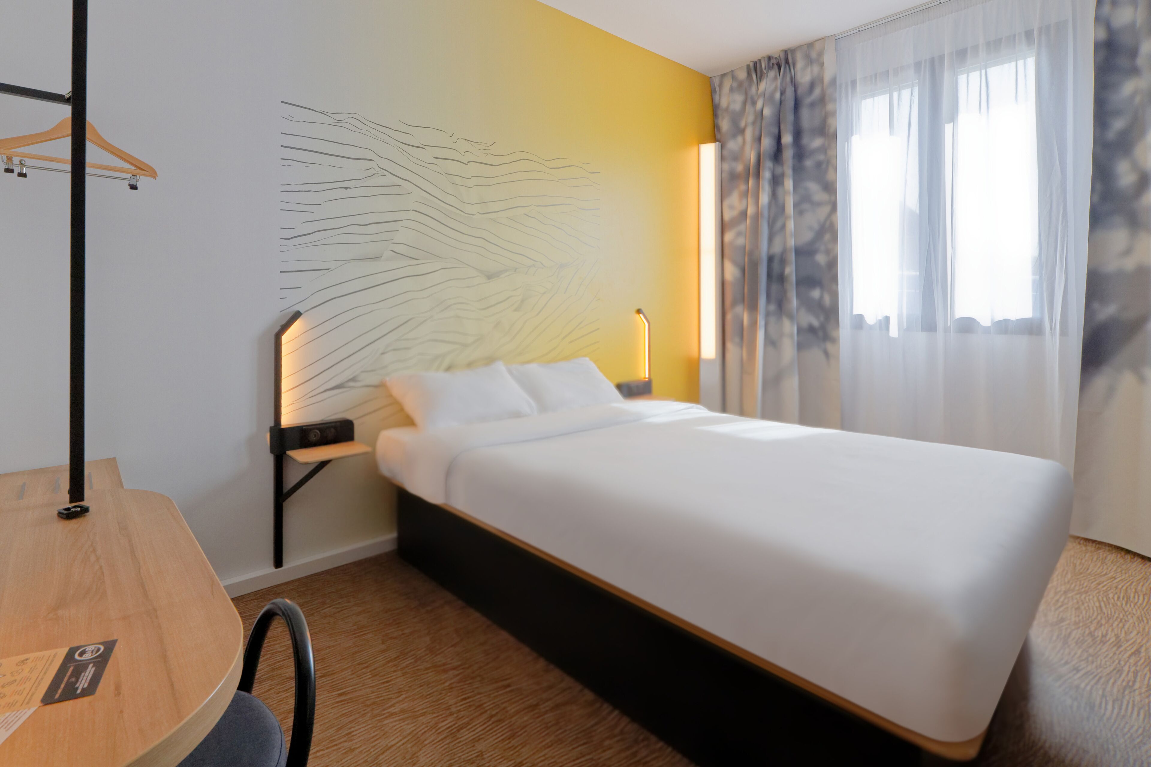 A hotel room with a bed, a desk, and a chair.