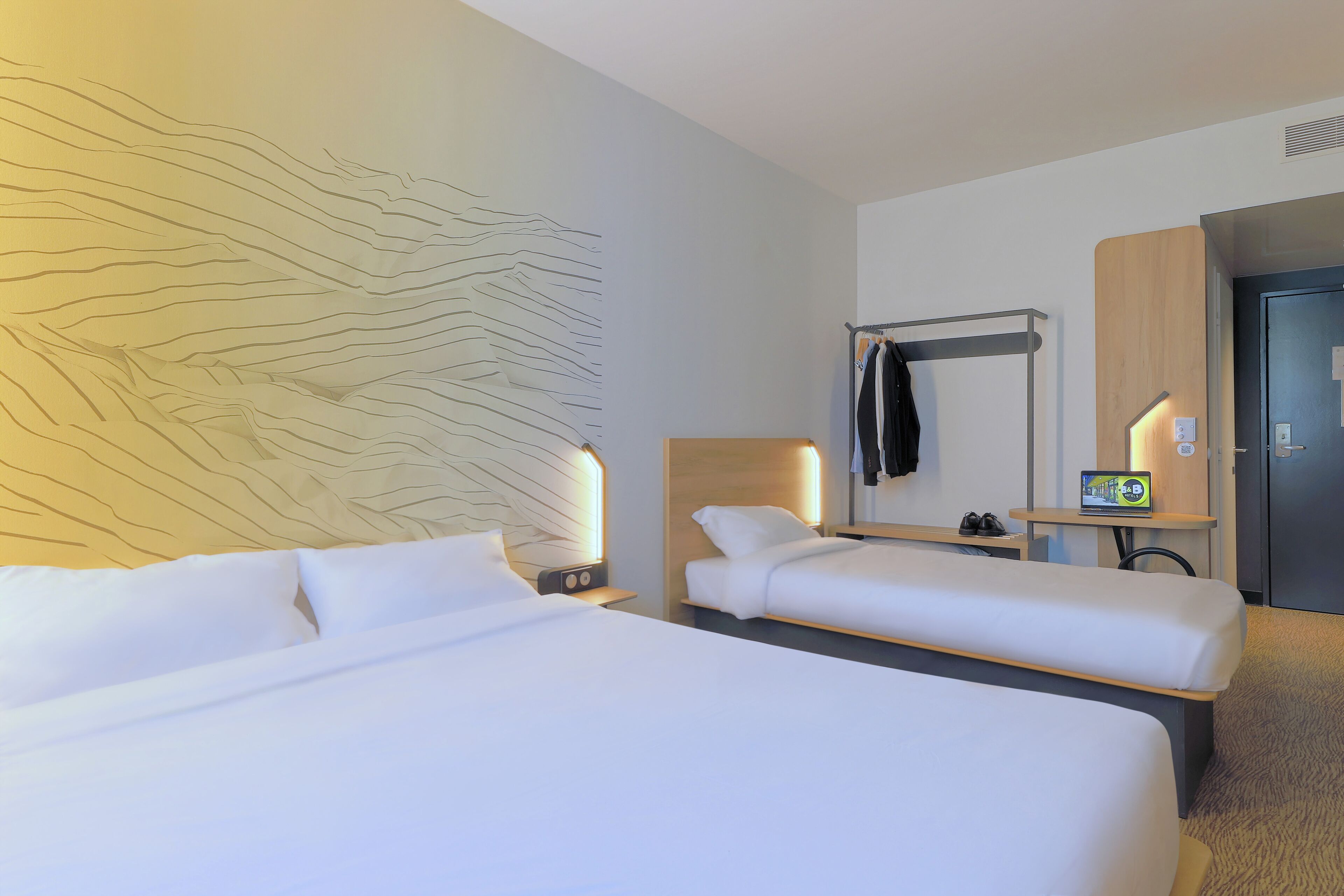 Une chambre d’hôtel avec deux lits, une œuvre d’art murale, un porte-manteau, une télévision et une porte.