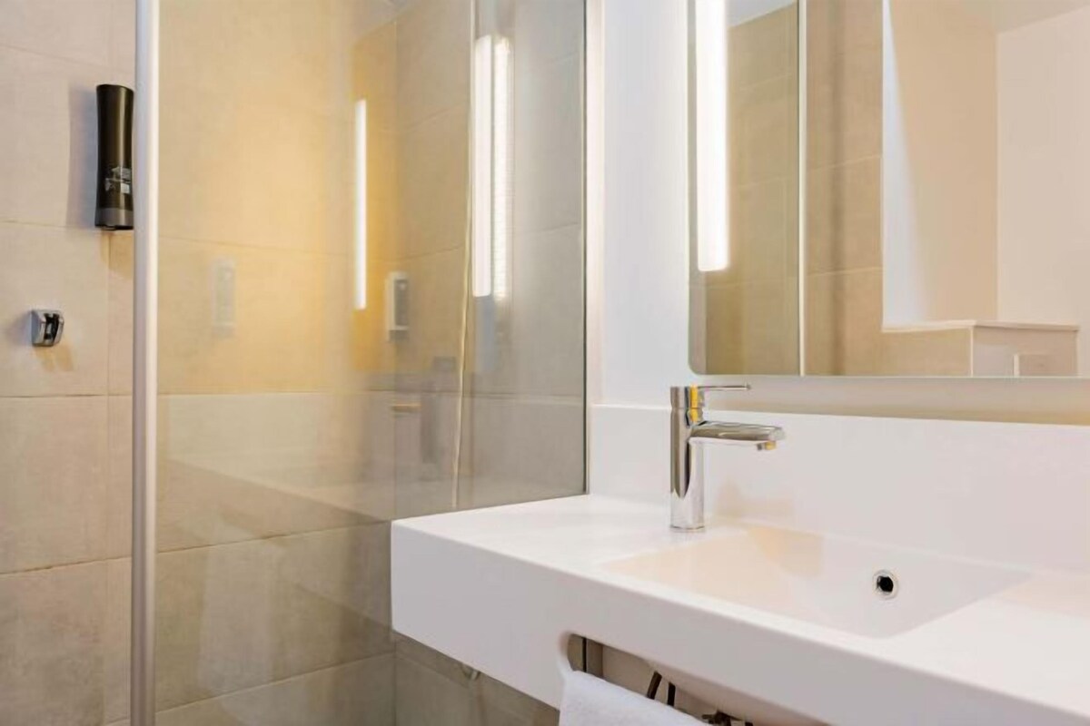 Une salle de bain moderne avec un lavabo blanc, un miroir et une cabine de douche en verre.