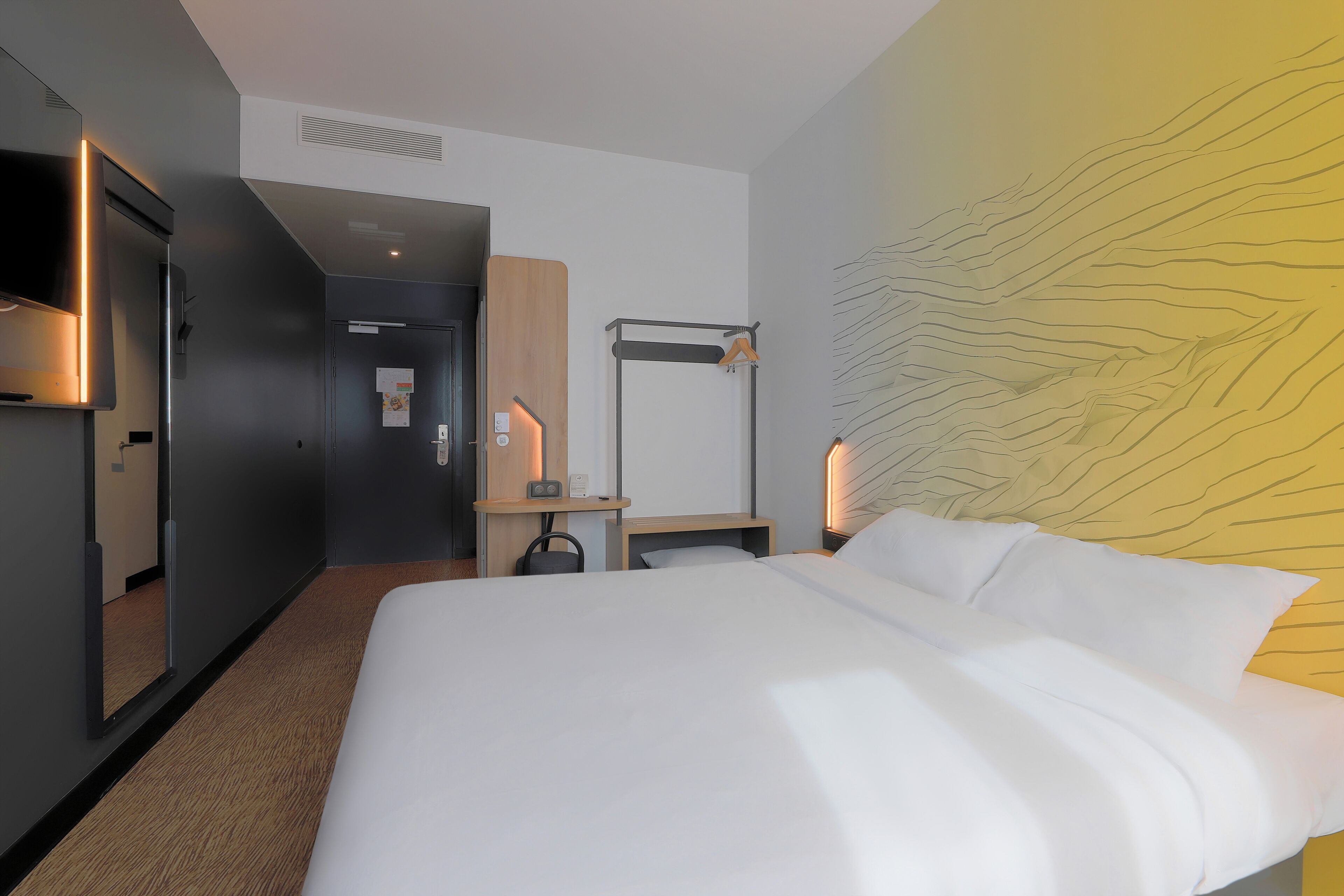 Habitación de hotel con una cama grande, un escritorio, una silla, un televisor y una pared con un diseño único.