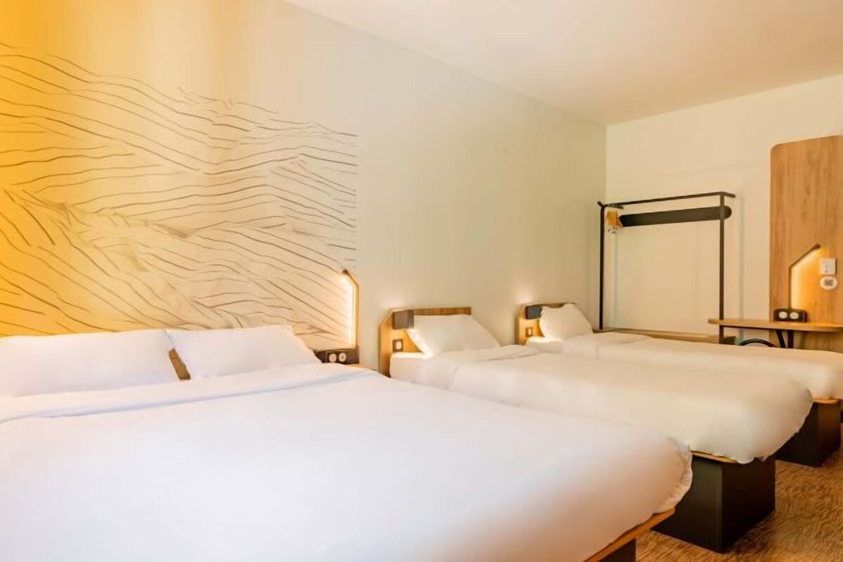 Une chambre d’hôtel avec deux lits, une grande œuvre d’art abstraite accrochée au mur, une tête de lit en bois et un miroir avec un cadre en bois.