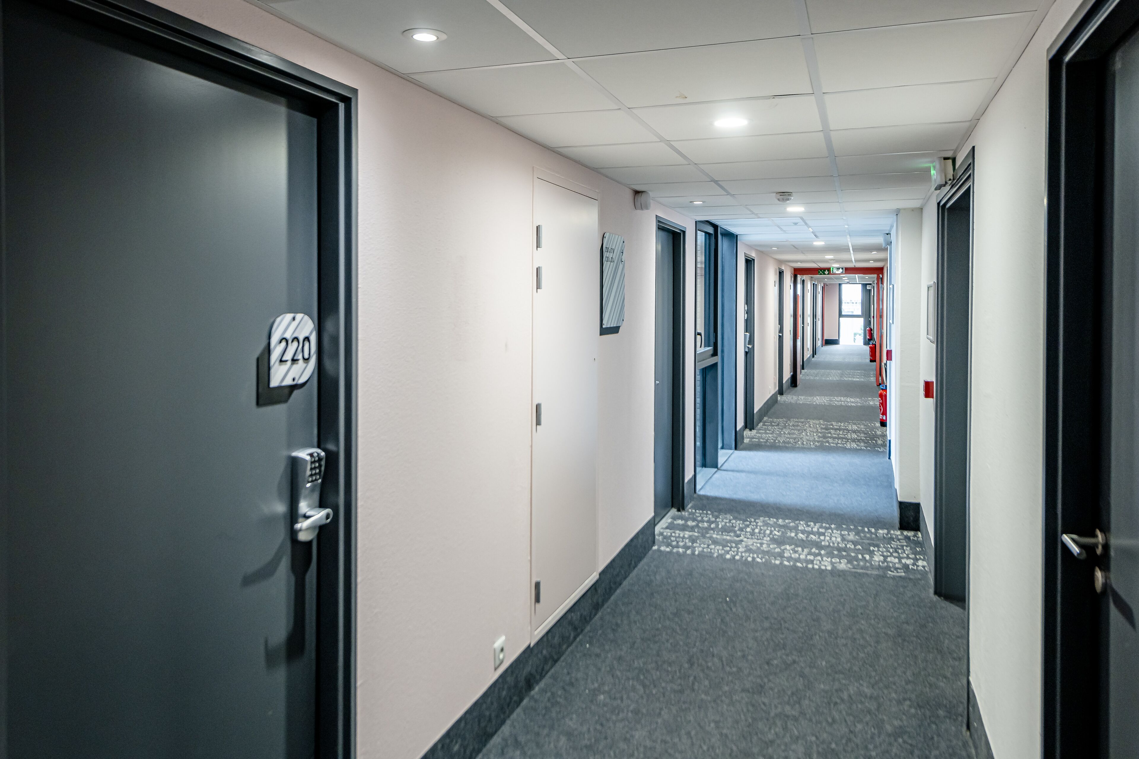 Un couloir avec les portes numérotées 220 et 221, un sol recouvert de moquette et un plafond doté d’un éclairage encastré.
