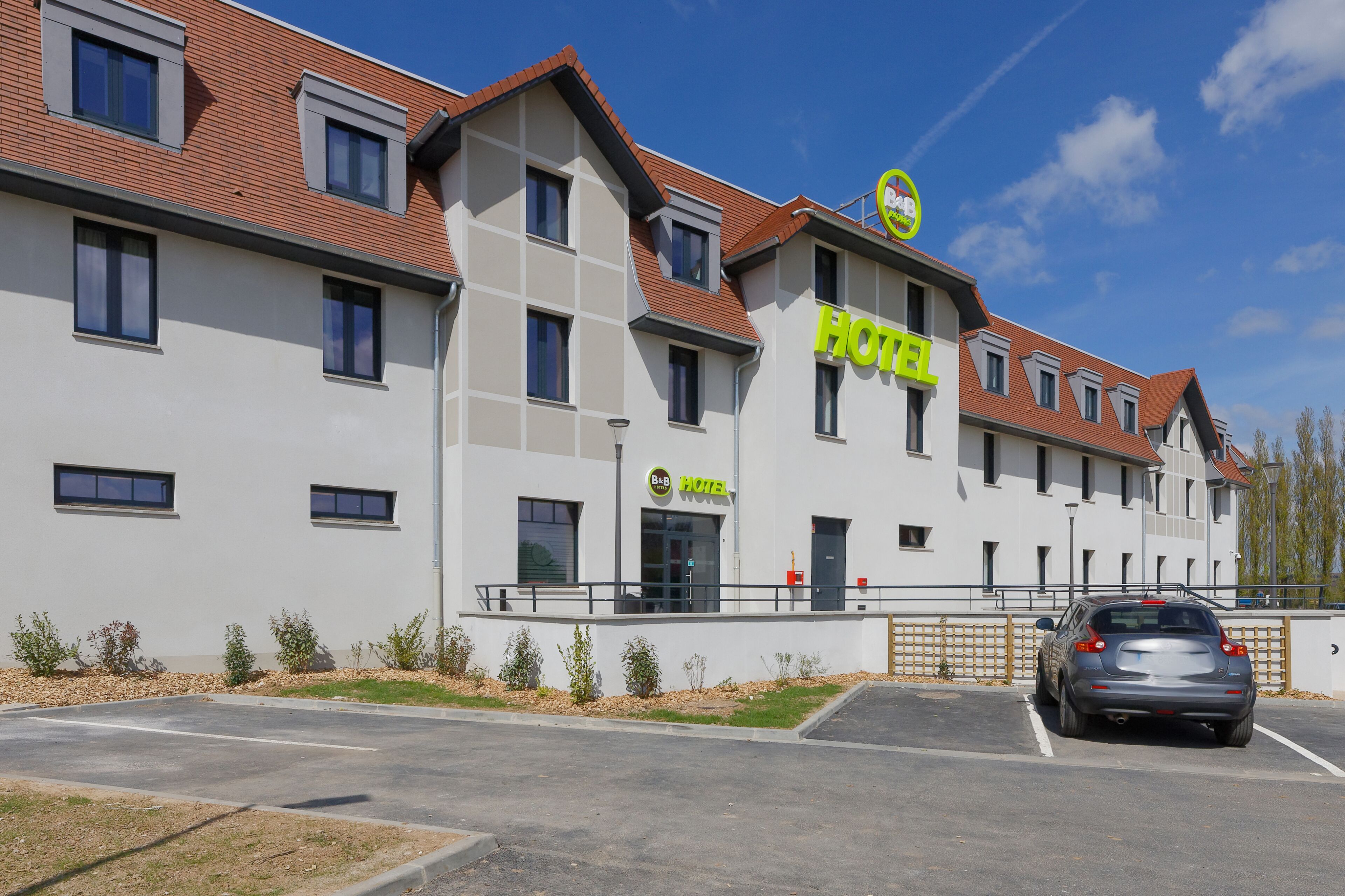 A modern hotel with a flat roof, multiple windows, and a parking lot.