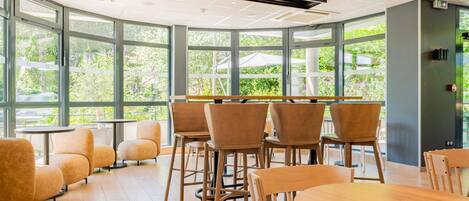 A modern indoor space with large windows, wooden tables and chairs, and a ceiling with recessed lighting.