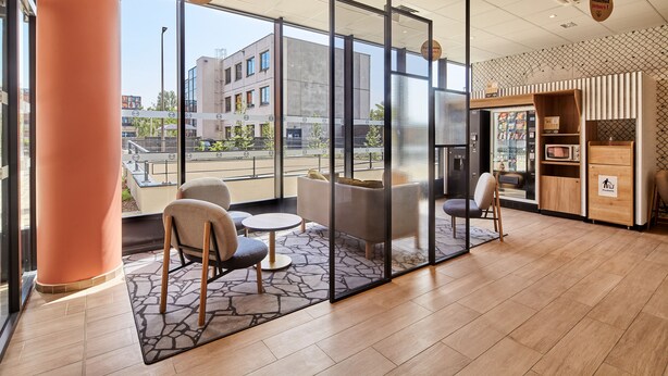 A modern interior with a seating area, a vending machine, and a view of the outside building. - B&B HOTEL Argenteuil (Argenteuil)