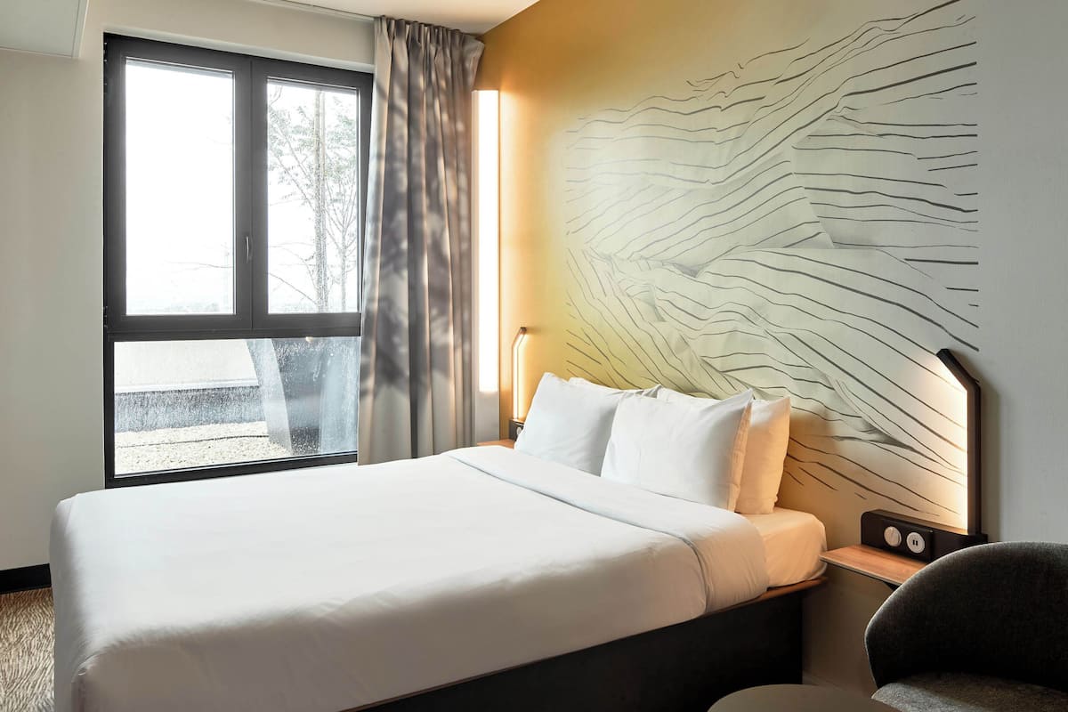 Habitación de hotel con una cama grande, una mesita de noche con lámpara, una silla y un diseño único en la pared.
