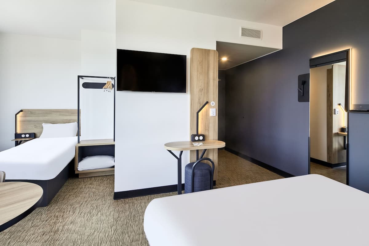 Habitación de hotel con dos camas, un televisor, una mesita con lámpara y un muro decorativo de madera.