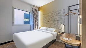 Una habitación de hotel moderna con una cama grande, una mesita, un perchero y una ventana con cortinas.