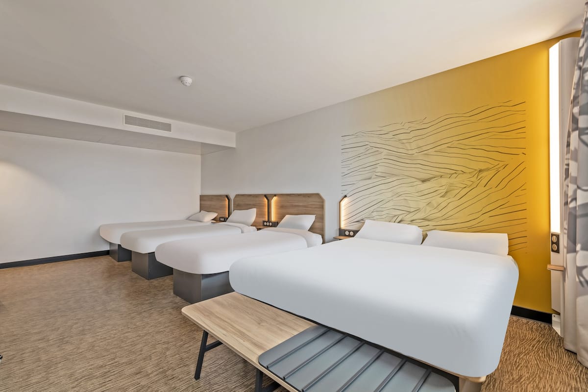 Une chambre d’hôtel avec trois lits, un banc en bois et une grande œuvre d’art abstraite accrochée au mur.