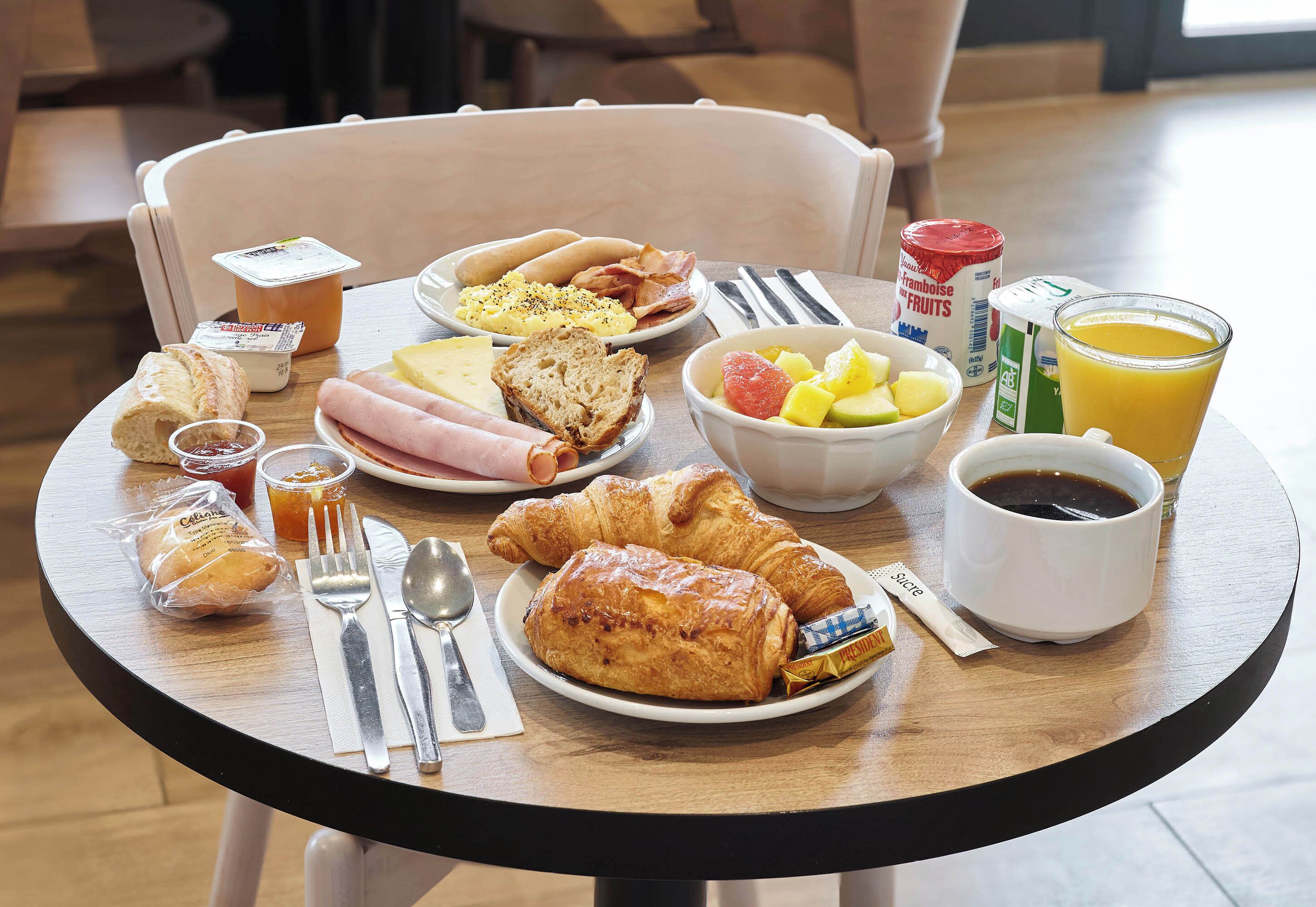 A breakfast table with croissants, ham, bread, fruit, and a cup of coffee.