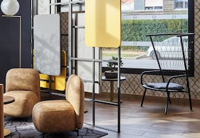 A modern interior with two leather armchairs, a small round table, a yellow partition, and a view of a parking lot through a window with a metal grid.