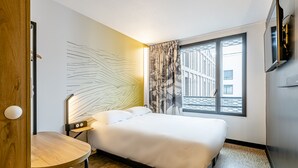 A hotel room with a bed, a desk, a chair, a TV, and a window with a view of buildings. - B&B HOTEL Bois D'Arcy Saint Quentin en Yvelines (Bois-d'Arcy)
