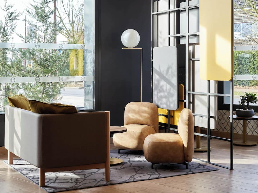 Una sala de estar moderna con sofá, sillón, reposapiés, una lámpara de pie y vistas amplias a través de grandes ventanales.