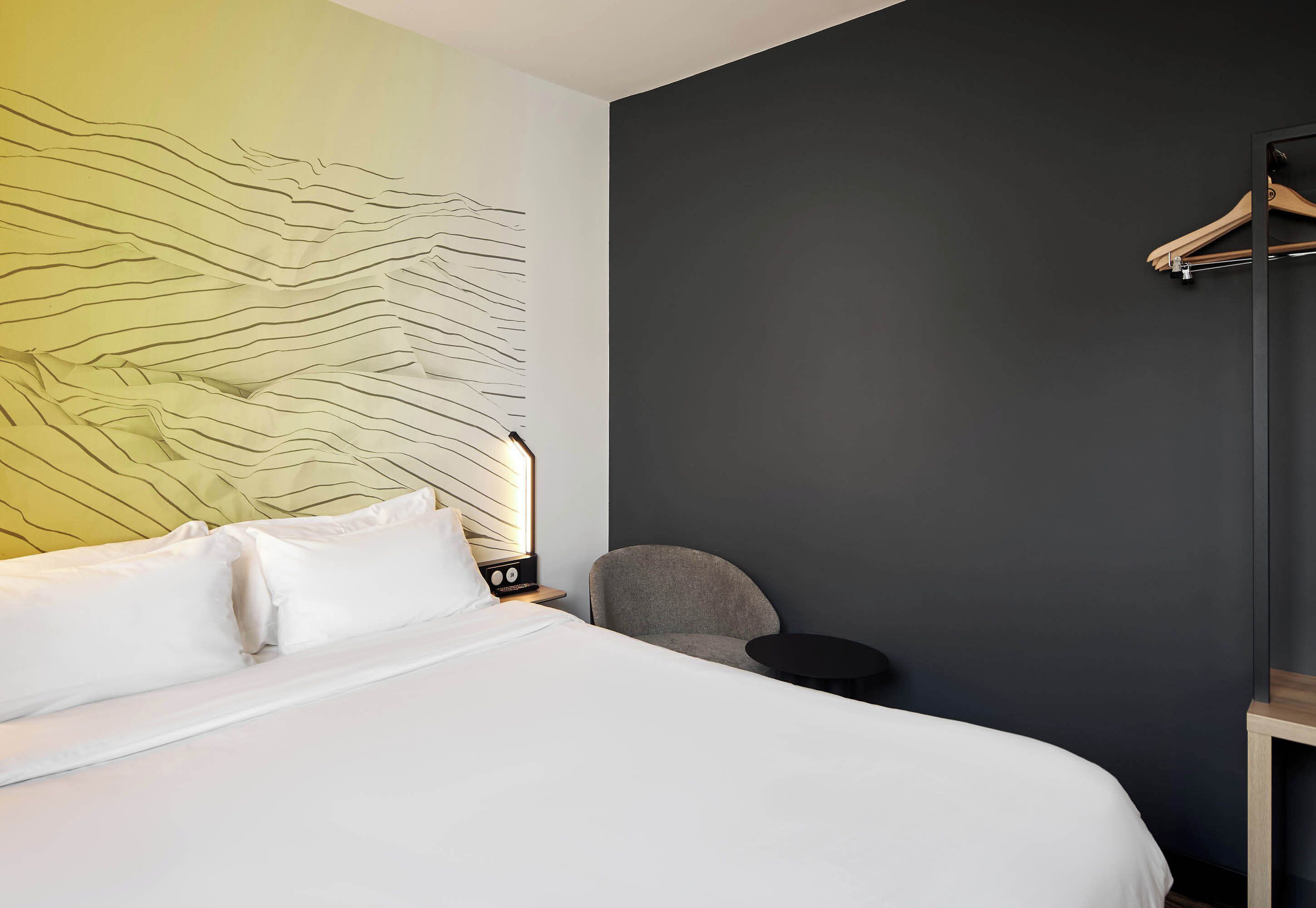 Ein Hotelzimmer mit einem Bett, einem Sessel, einem kleinen Tisch und einem Kleiderständer.