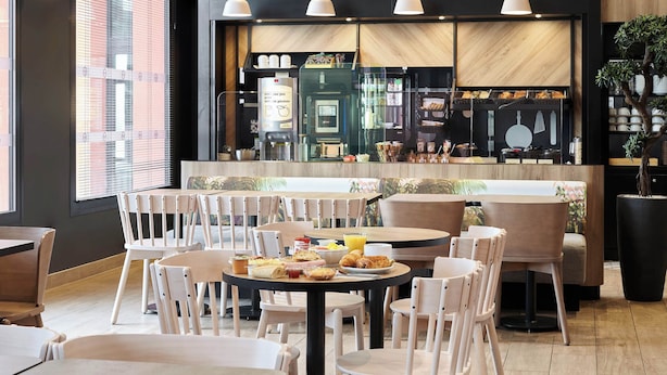 A modern cafe with round tables and white chairs, a coffee machine, and a menu board. - B&B HOTEL Bois D'Arcy Saint Quentin en Yvelines (Bois-d'Arcy)
