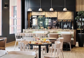 A modern cafe with round tables and white chairs, a coffee machine, and a menu board.