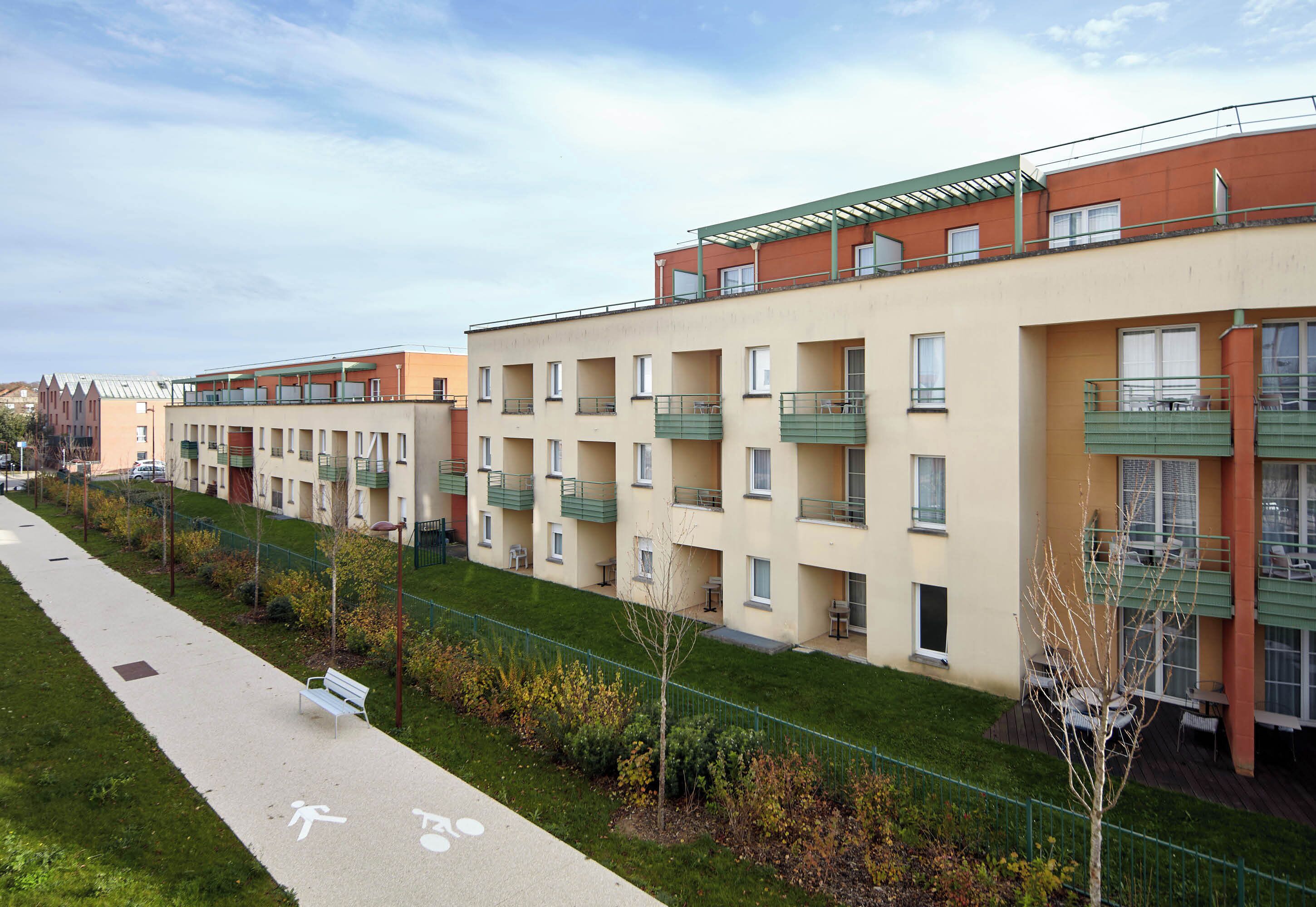 Una hilera de modernos edificios de apartamentos con balcones, un sendero peatonal y un pequeño parque.
