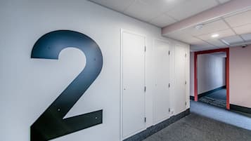 Un pasillo con un gran número 2 en la pared, puertas blancas y un vano de entrada con marco rojo al final.