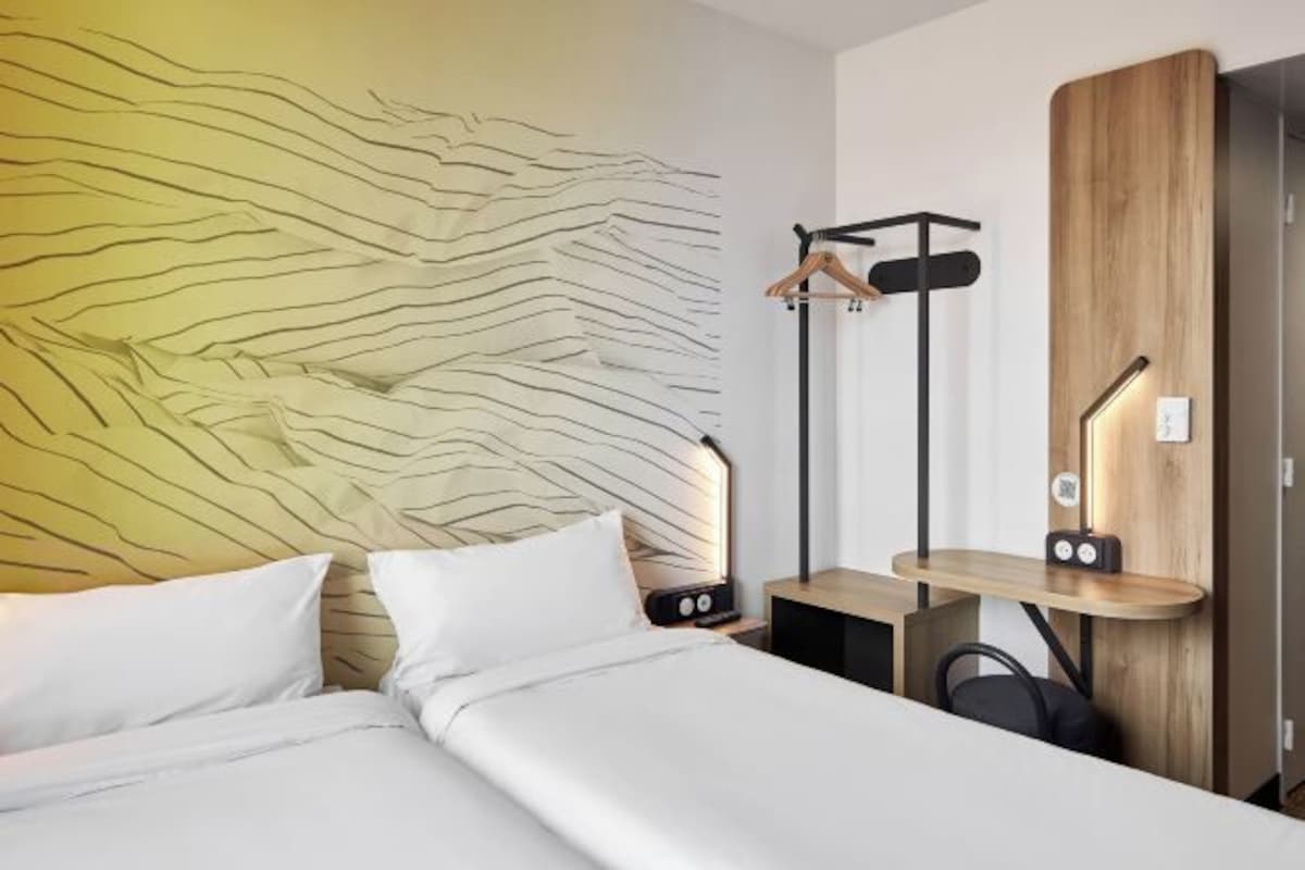 A modern hotel room with a bed, bedside table, and a wooden wardrobe.