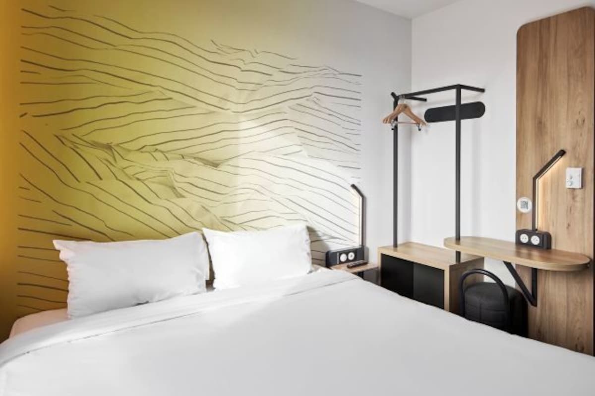 A modern hotel room with a bed, a desk, a chair, and a unique wall design.