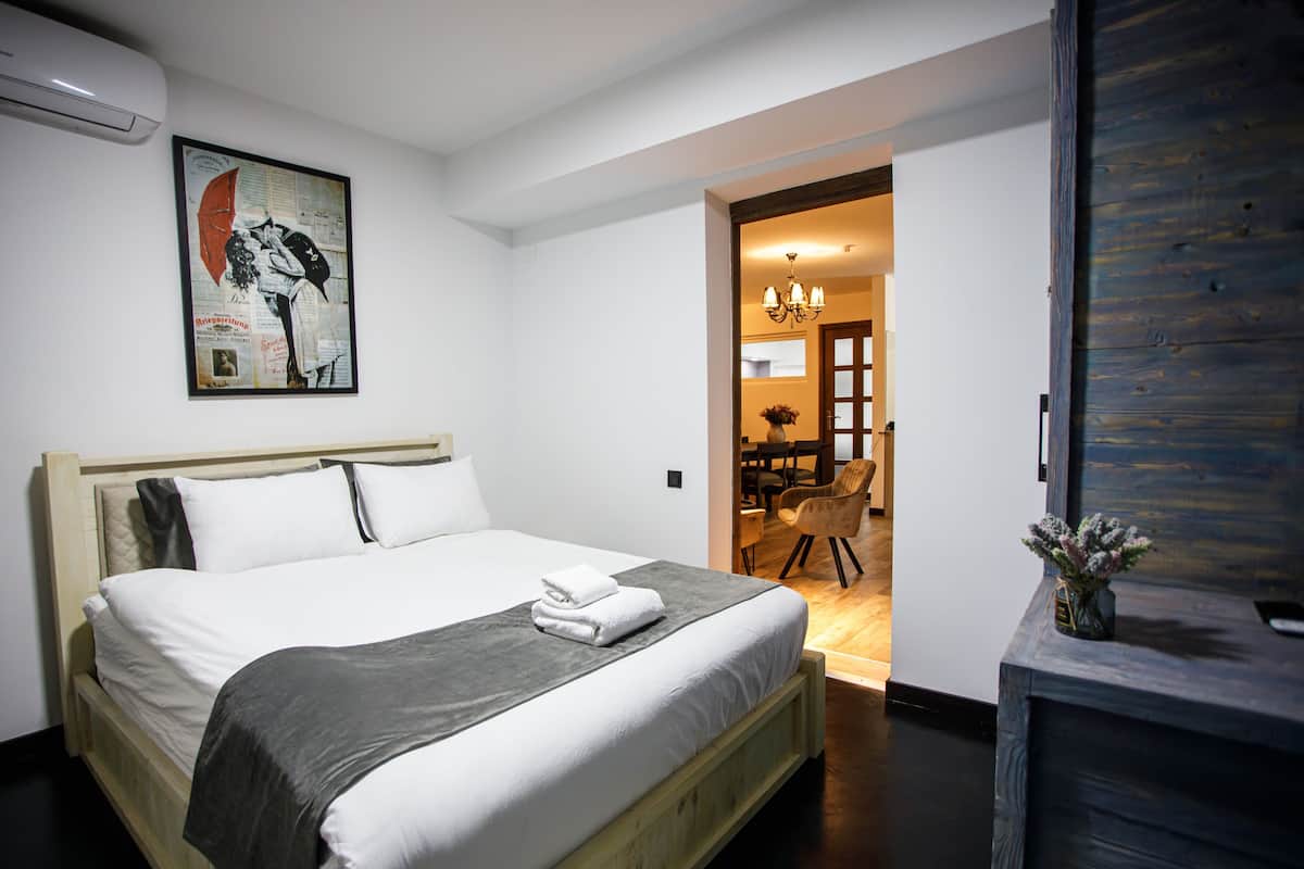 A bedroom with a bed, a painting, a desk, and a chair.