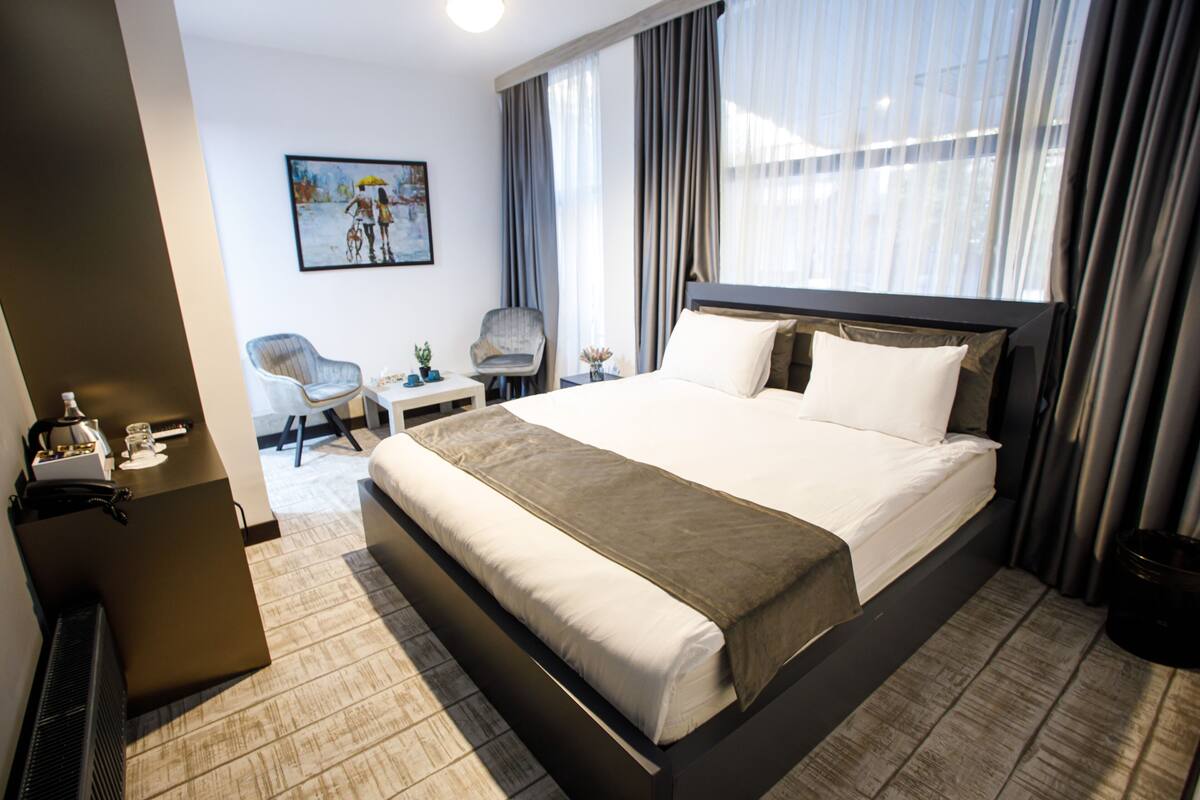 A hotel room with a large bed, a chair, a small table, and a painting on the wall.