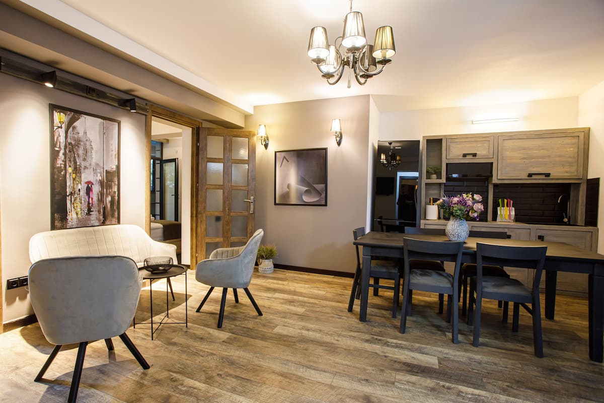 A modern kitchen with a dining area, wooden flooring, and a chandelier.